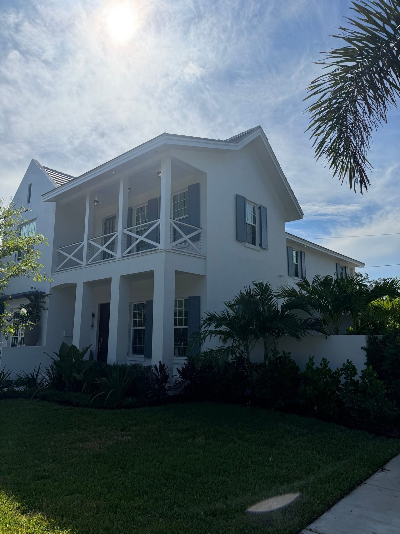 Custom home exterior with balcony and shutters framed by palm trees