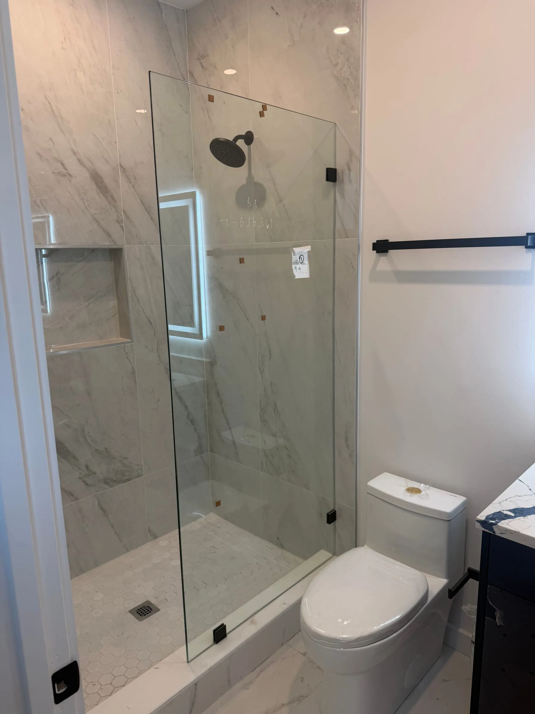Glass-enclosed shower with marble-look tile and niche