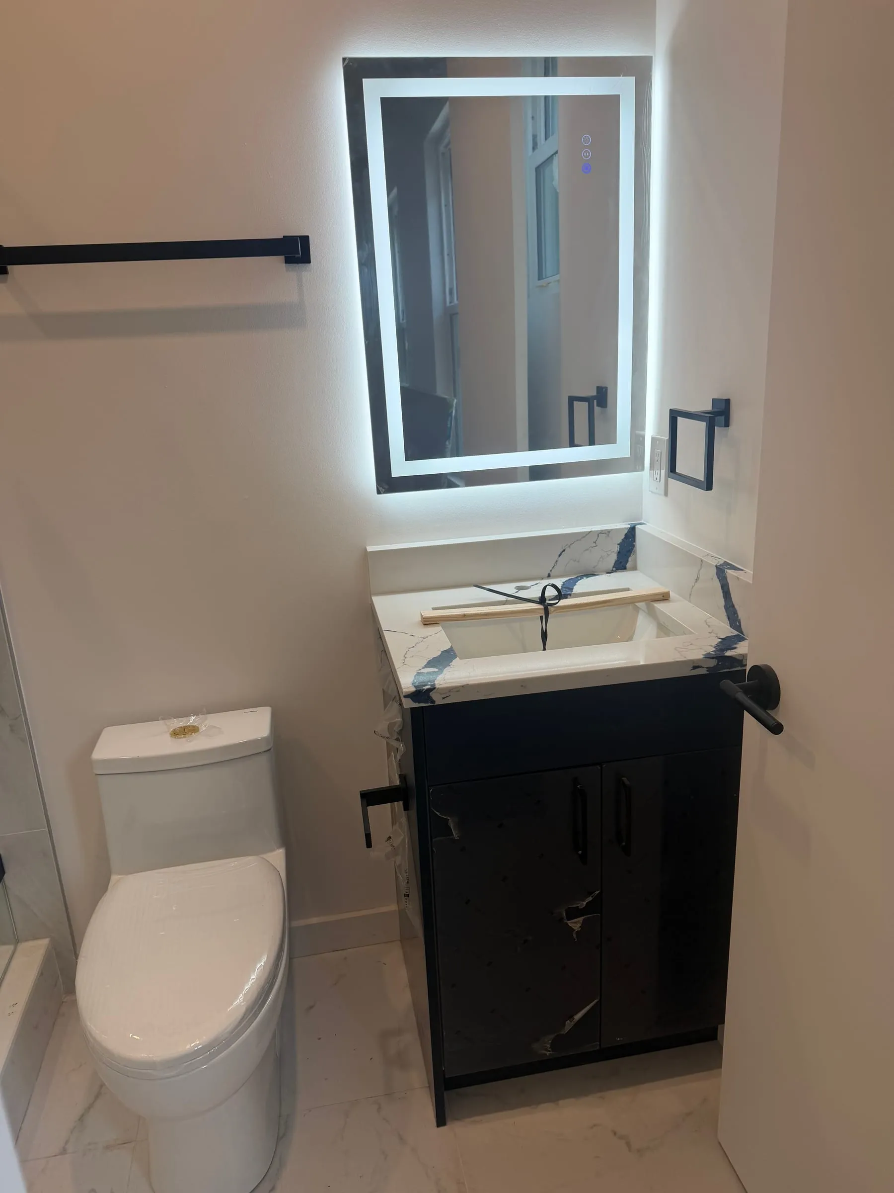 Powder room with black vanity and lit mirror
